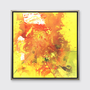 A yellow, orange and white abstract print in a silver floater frame hangs on a white wall.
