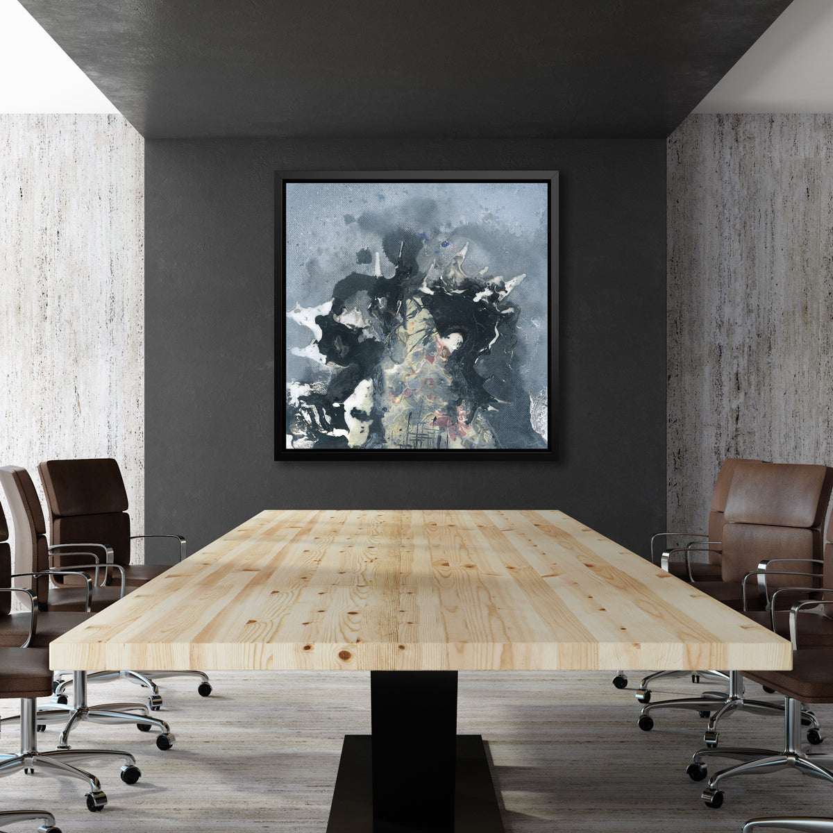 A grey, black, white and light yellow abstract print in a black floater frame hangs on a dark grey wall across from a long wood table with several brown leather desk chairs.