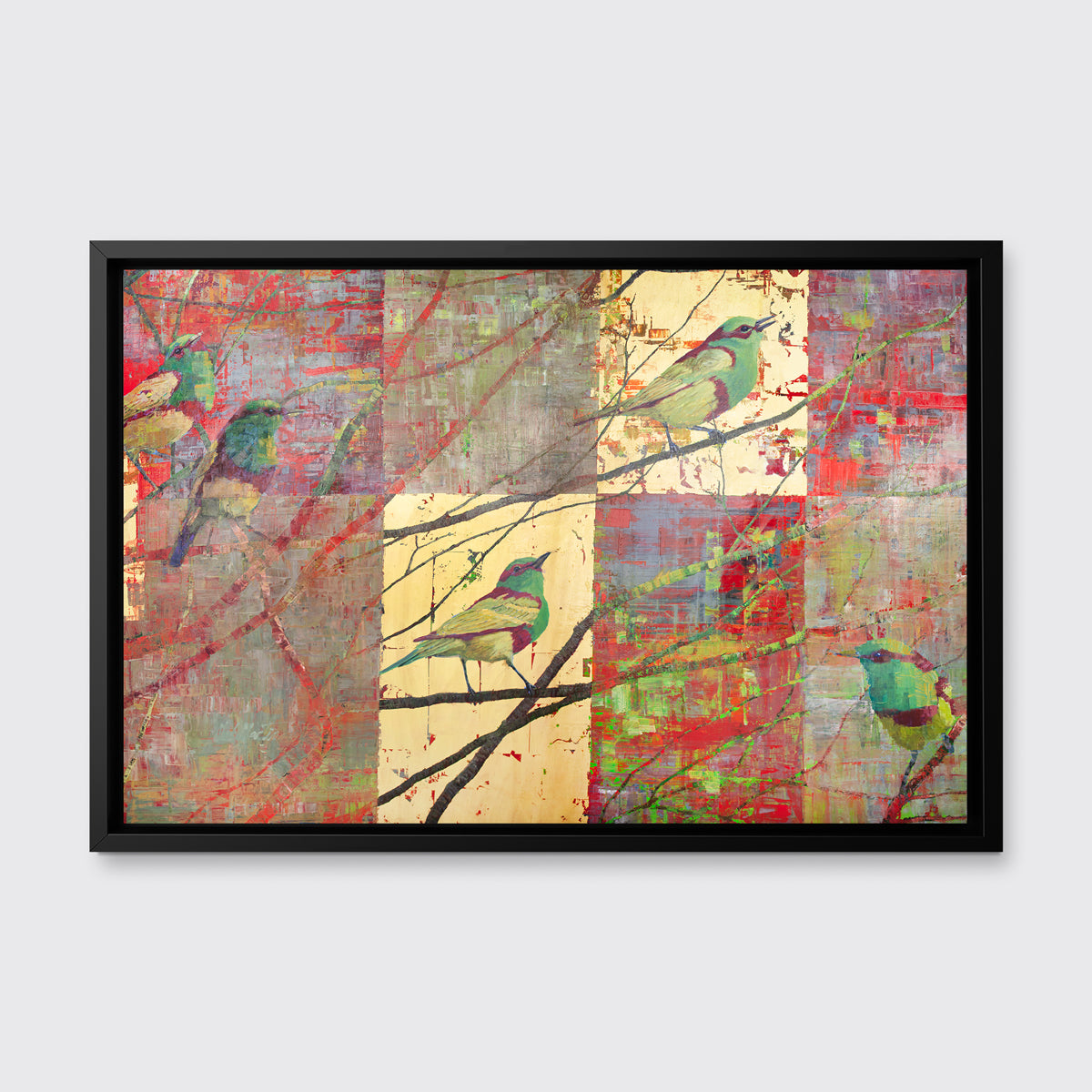 A red, gold and green geometric abstract print of birds in a tree in a black floater frame hangs on a white wall.