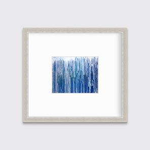 A blue and white abstract print in a silver frame with a mat hangs on a white wall.