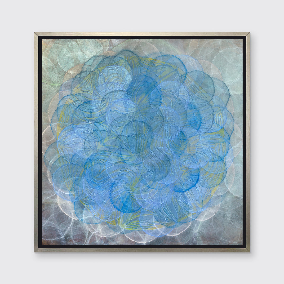 A silver, grey and blue abstract overlapping circle print in a silver floater frame hangs on a white wall.
