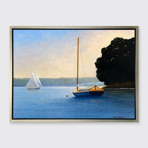 A blue, beige and black contemporary seascape print with two sailboats in a silver floater frame hangs on a white wall.