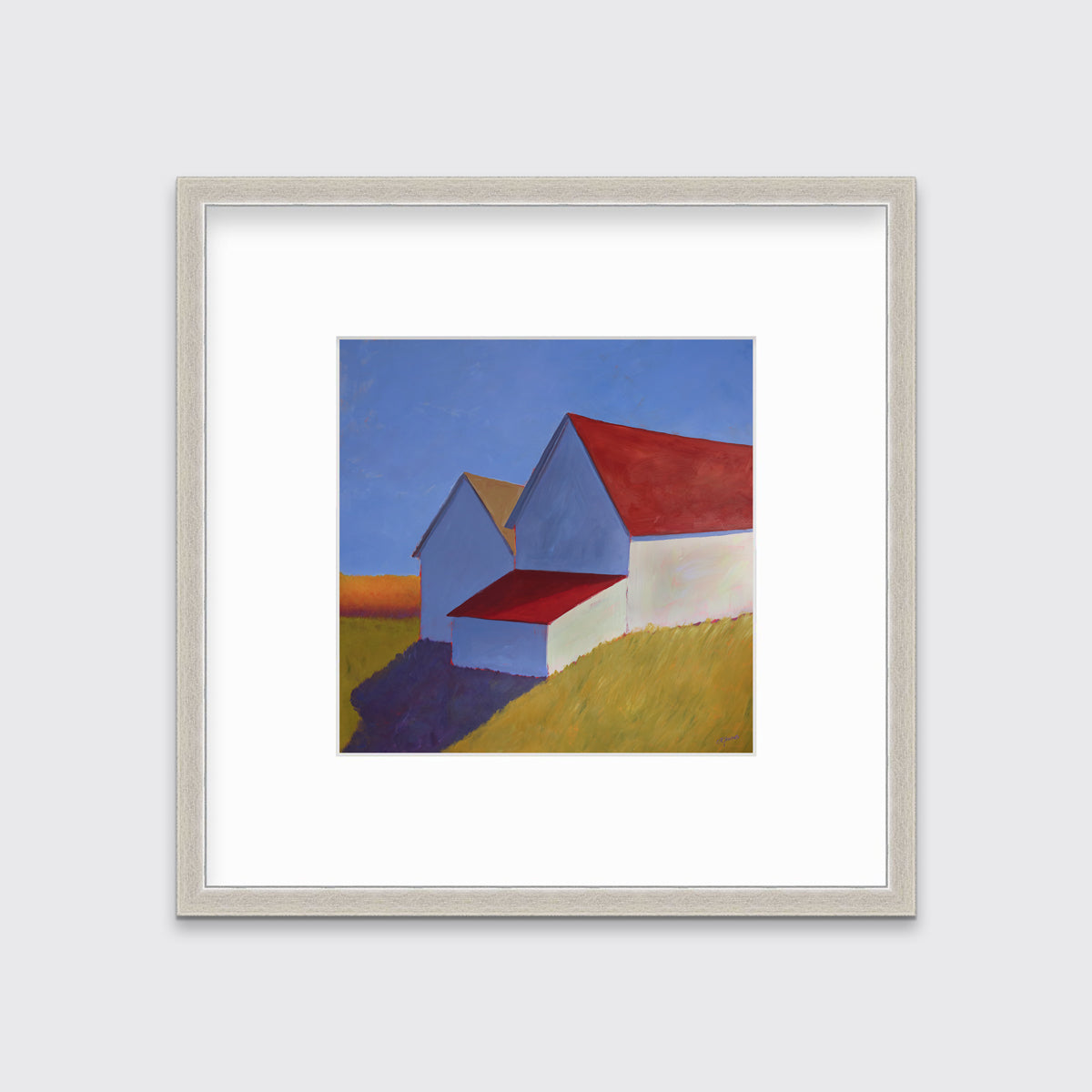 A white barn with a red roof print in a silver frame with a mat hangs on a white wall.