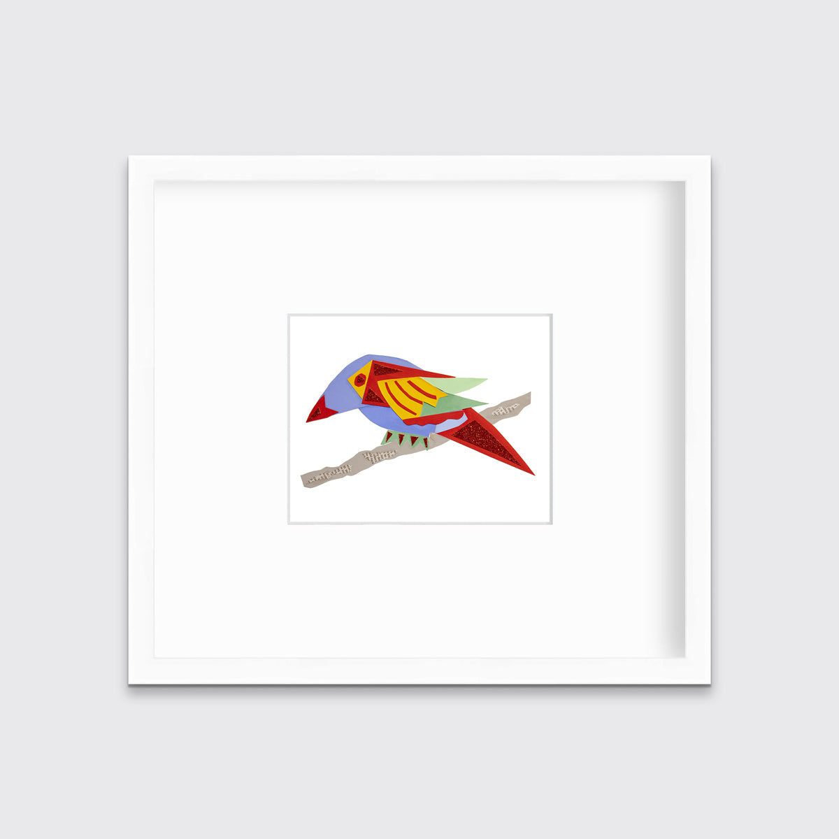A multicolored bird on a branch collage print in a white frame with a mat hangs on a white wall.