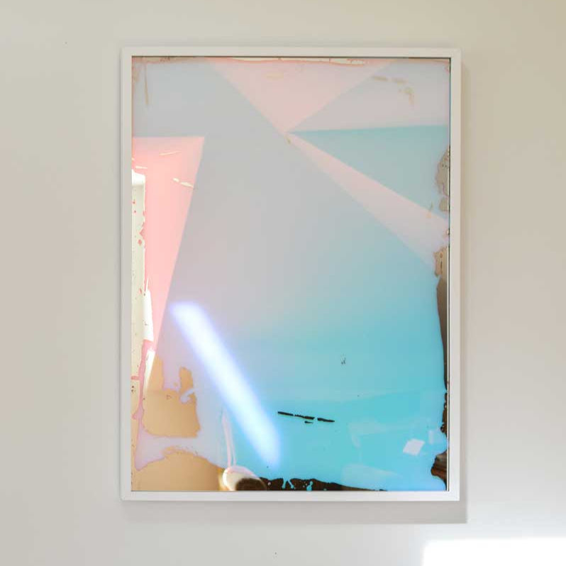 A multi-colored fine art mirror hangs on a white wall.
