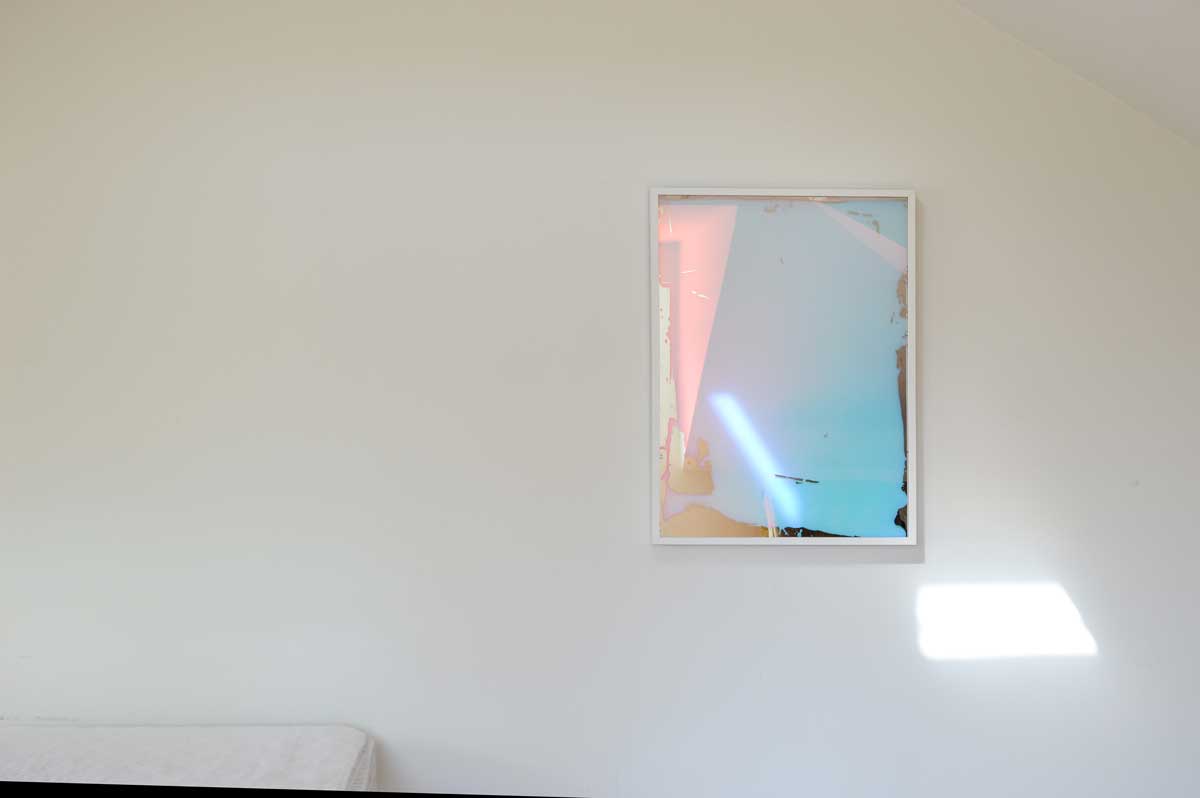 A multicolored fine art mirror framed in a white frame hangs on a white wall.