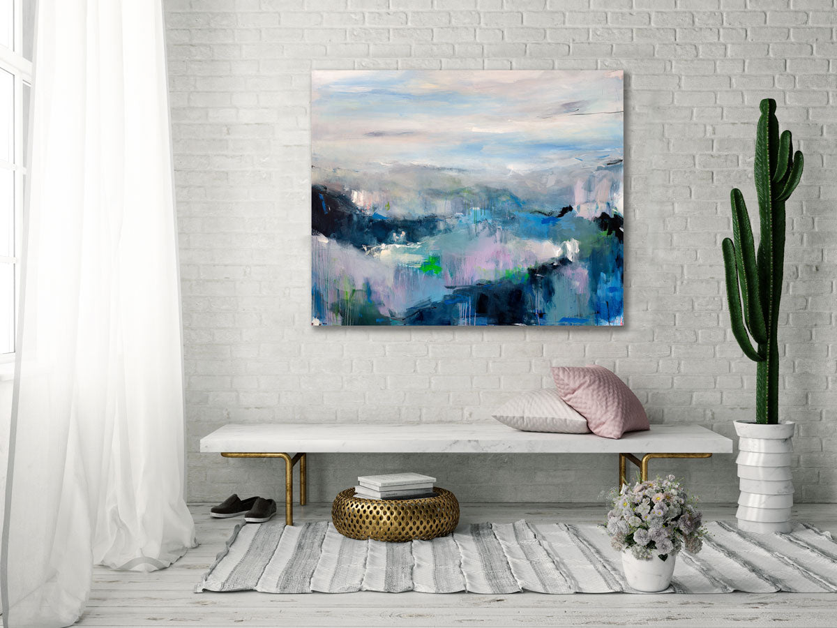 A colorful abstract landscape painting by Kelly Rossetti hangs above a marble bench with pillows, a tall potted cactus to the right and a grey and white rug.