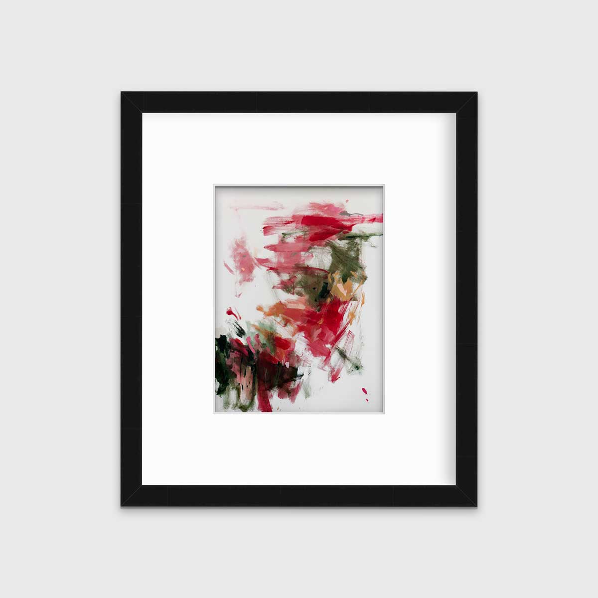 A red, green and white abstract print in a black frame with a mat hangs on a white wall.