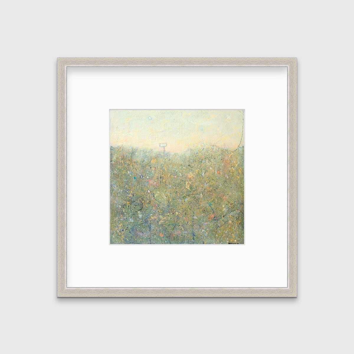 A yellow-green abstract landscape in a silver frame with a mat hangs on a white wall.