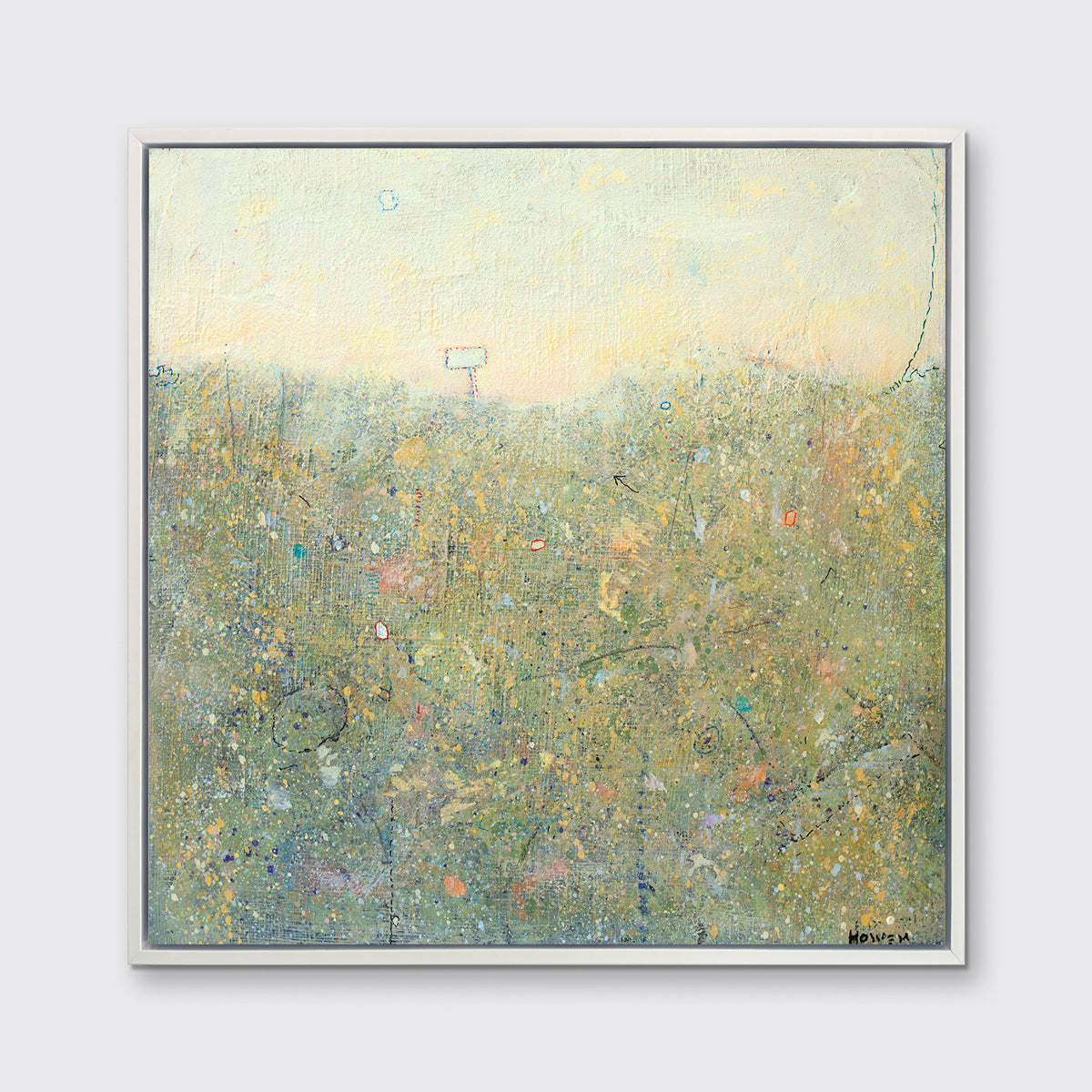 A light yellow and green abstract landscape print in a white floater frame hangs on a white wall.