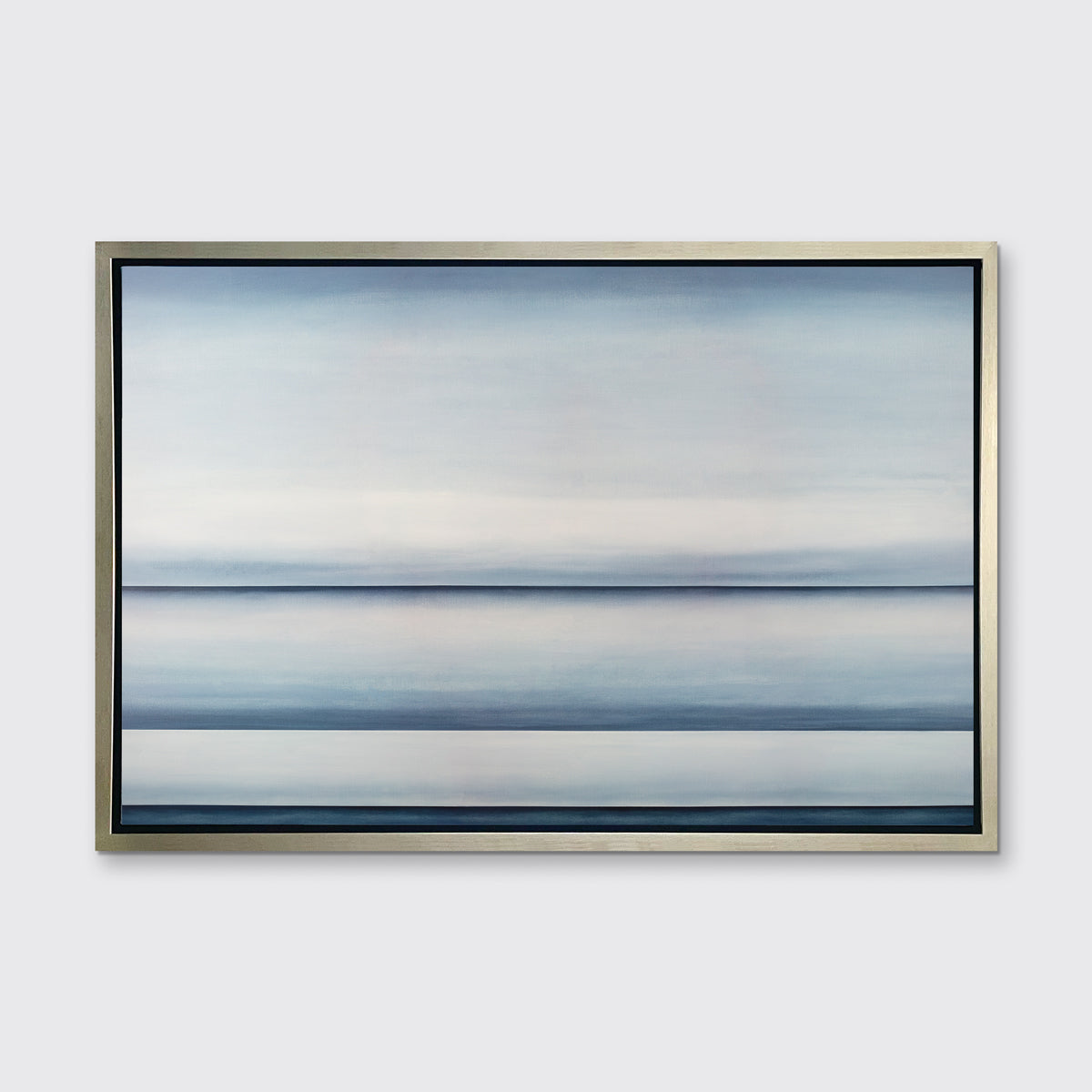 A tonal blue abstract landscape print in a silver floater frame hangs on a white wall.
