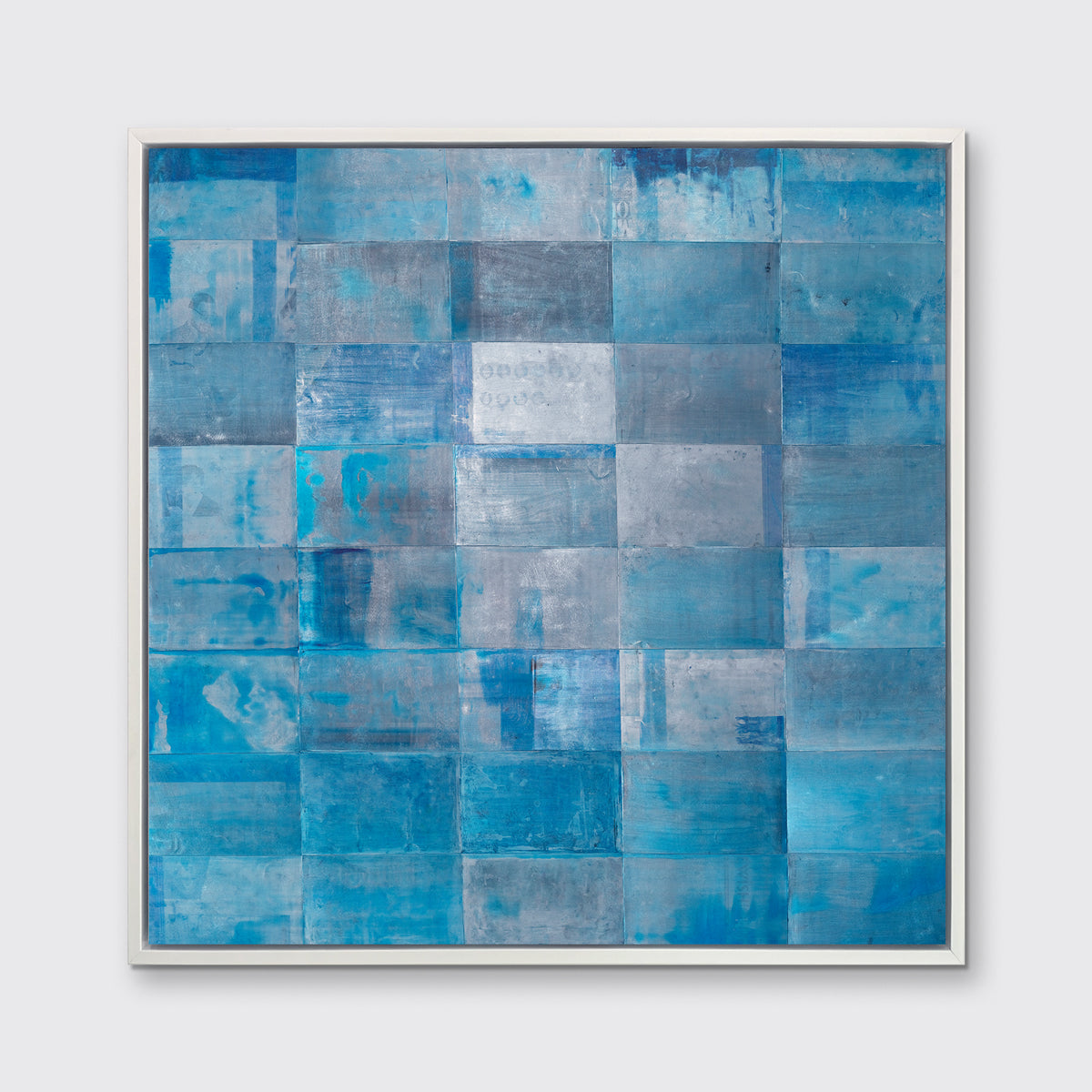 A blue geometric print in a white floater frame hangs on a white wall.