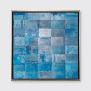 A blue geometric print with grey and silver accents in a silver floater frame hangs on a white wall.