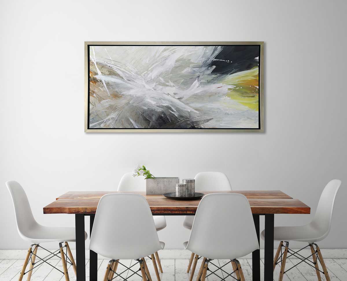 A white, black, grey and gold abstract print in a silver floater frame hangs on a white wall above a live edge wood table and six white chairs.
