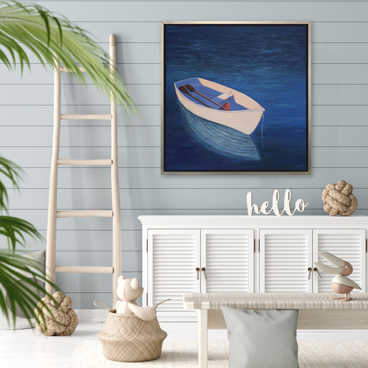 A blue, beige and lavender contemporary coastal print of a boat wading in the water in a silver floater frame hangs on a light teal shiplap wall above a white sideboard with decorative accents, a white bench and a ladder rests against the wall.