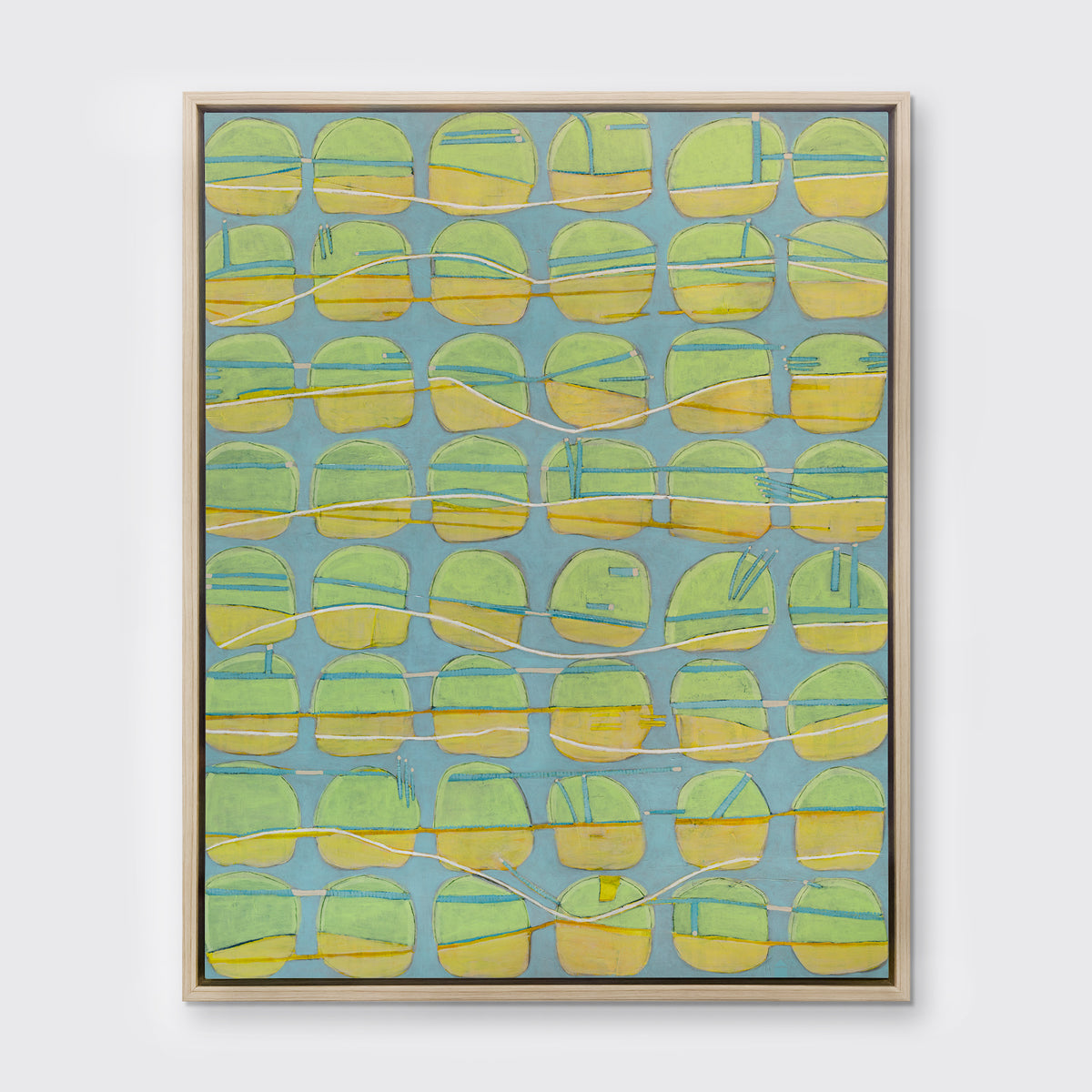 A yellow, green and light slate blue abstract circle print in a white oak wood floater frame hangs on a white wall.