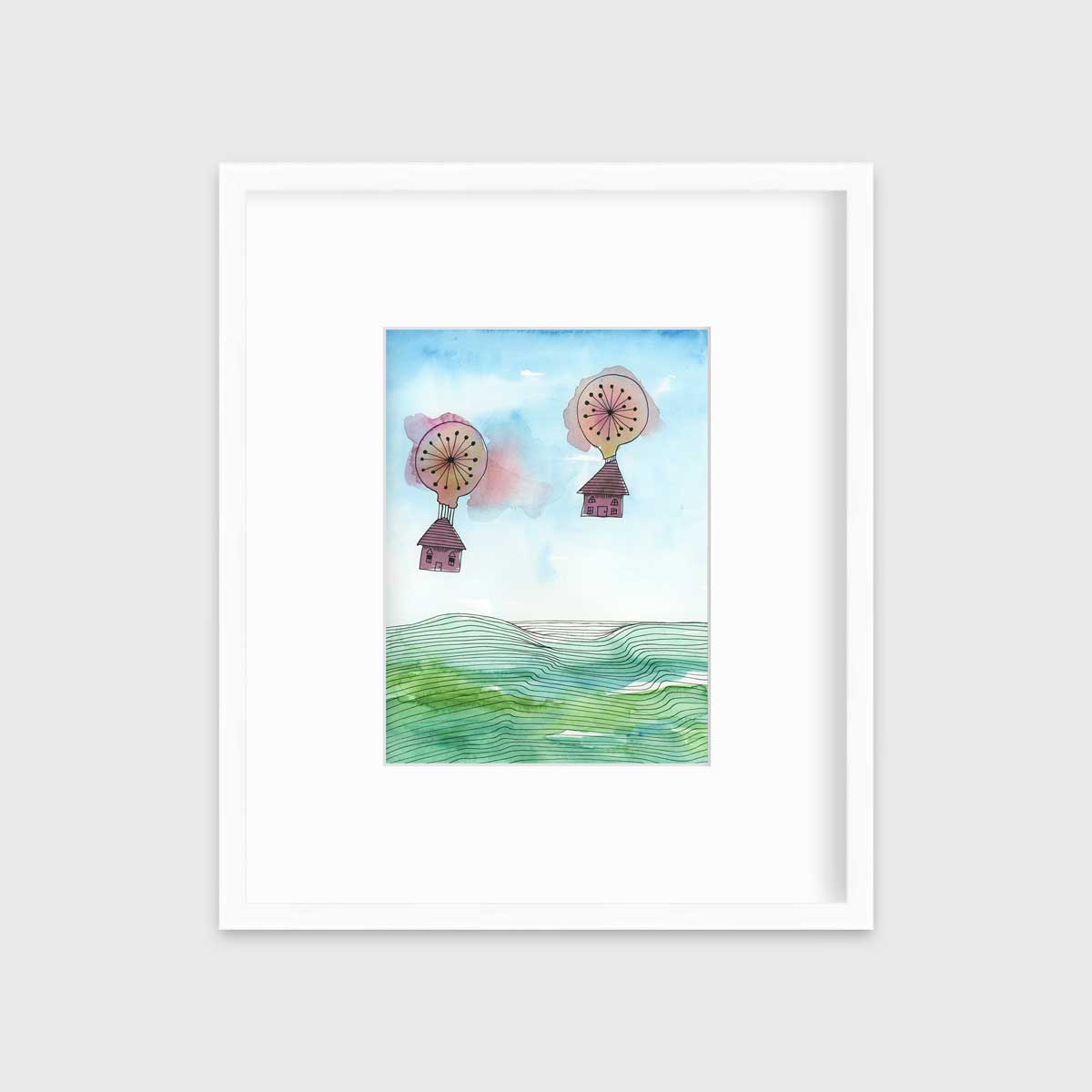 A hot air balloon and house illustration print in a white frame with a mat hangs on a white wall.