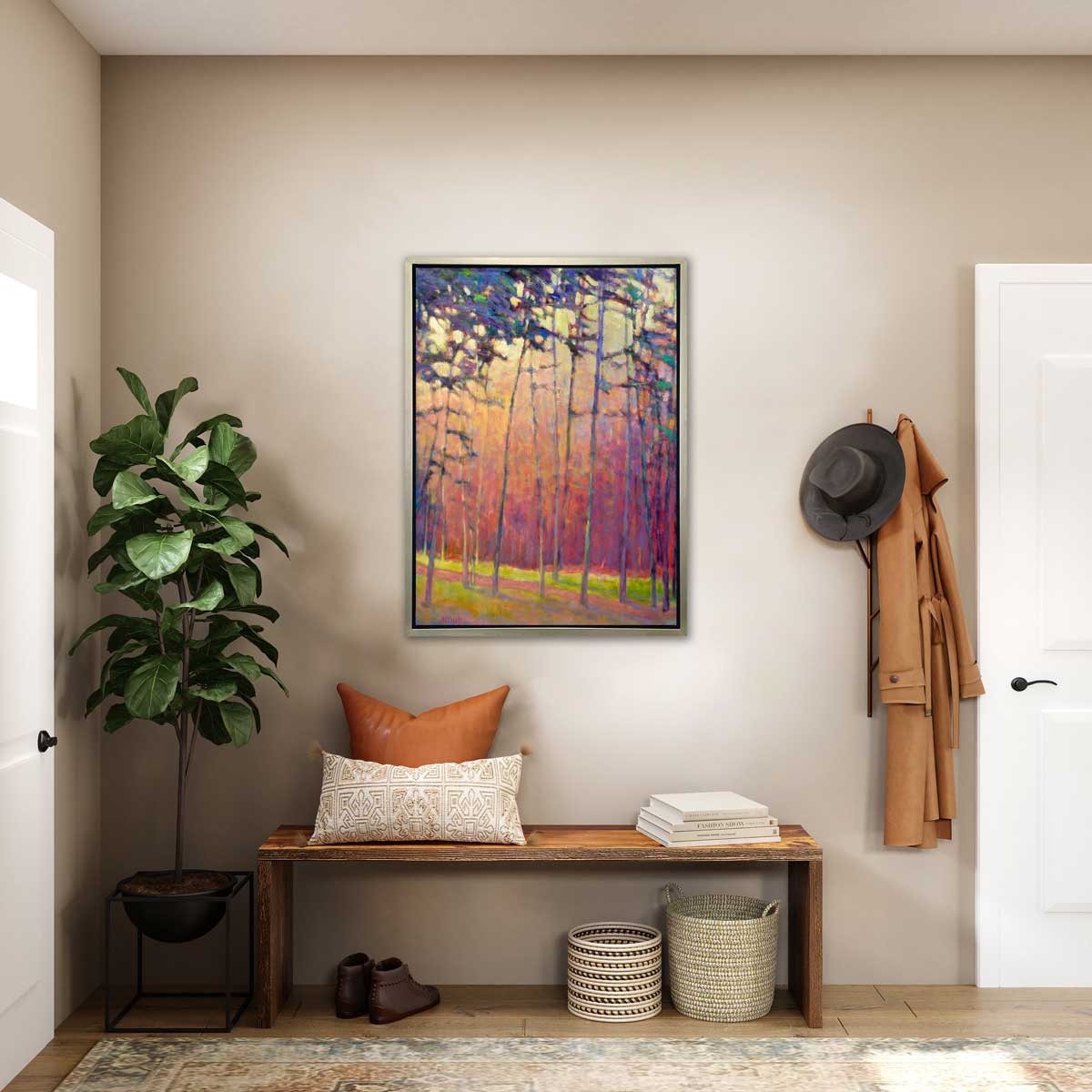 A red, orange and blue abstract tree landscape print in a silver floater frame hangs on a beige wall above wooden bench with pillows and stacked books, two woven baskets and brown shoes underneath, a potted floor plant and a wall coat hanger with a hat and a beige trench coat hanging.