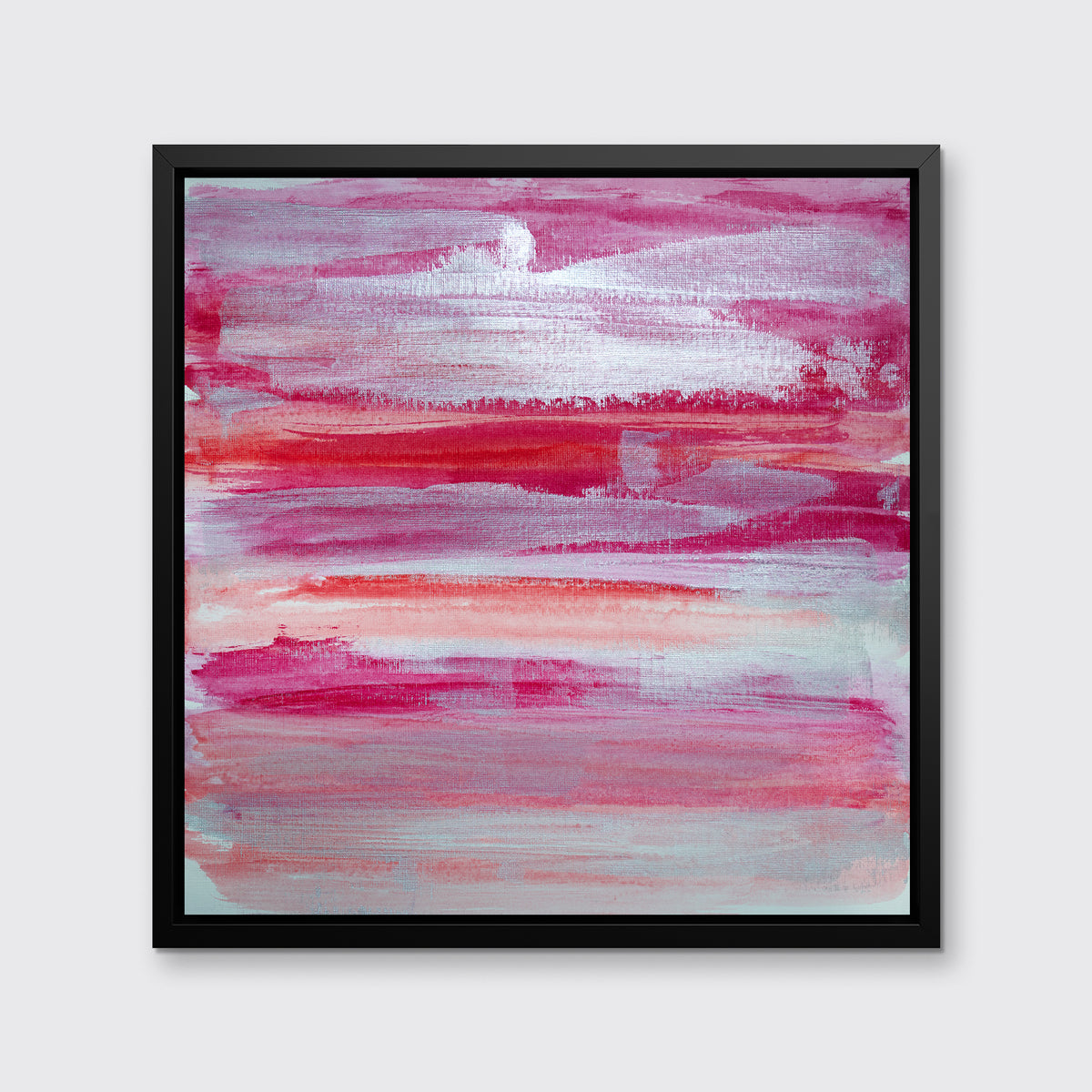 A pink, white, silver and red abstract print in a black floater frame hangs on a white wall.