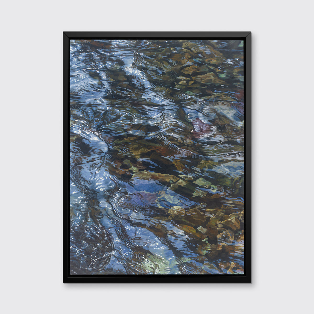 A brown, dark green, white and light blue abstract river rocks in water print in a black floater frame hangs on a white wall.