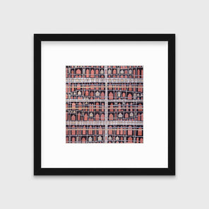 A pink, white and black abstract house print in a black frame with a mat hangs on a white wall.