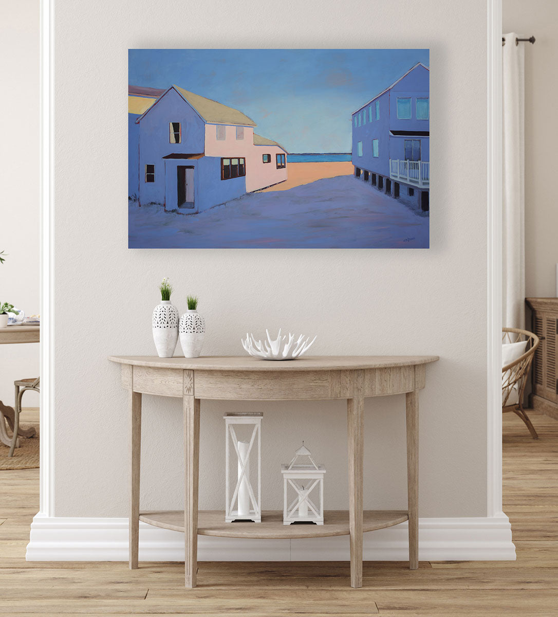 A purple contemporary landscape painting hangs on a white wall above a wooden half-moon console table with white lanterns and vases.