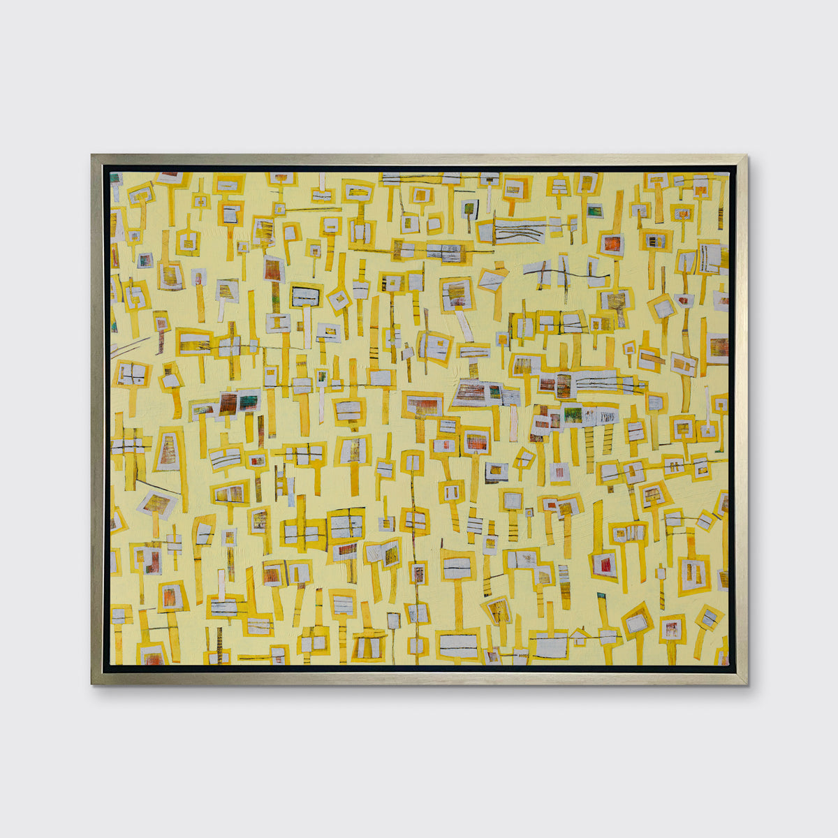 A yellow and grey abstract print in a silver floater frame hangs on a white wall.