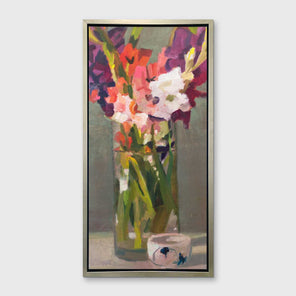 A purple, pink and green abstract floral print in a silver floater frame hangs on a white wall.