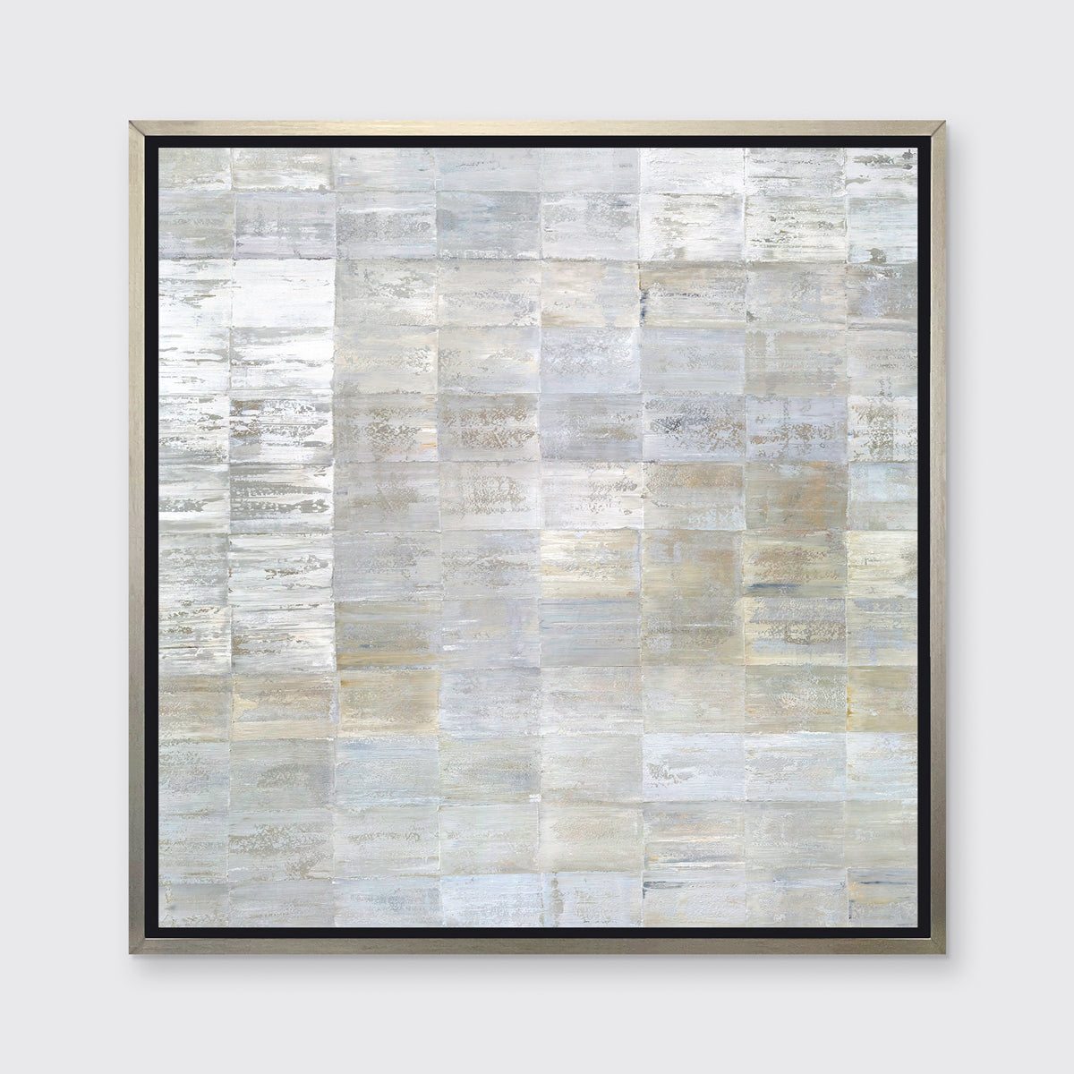 A grey, silver and light gold abstract geometric print in a silver floater frame hangs on a white wall.
