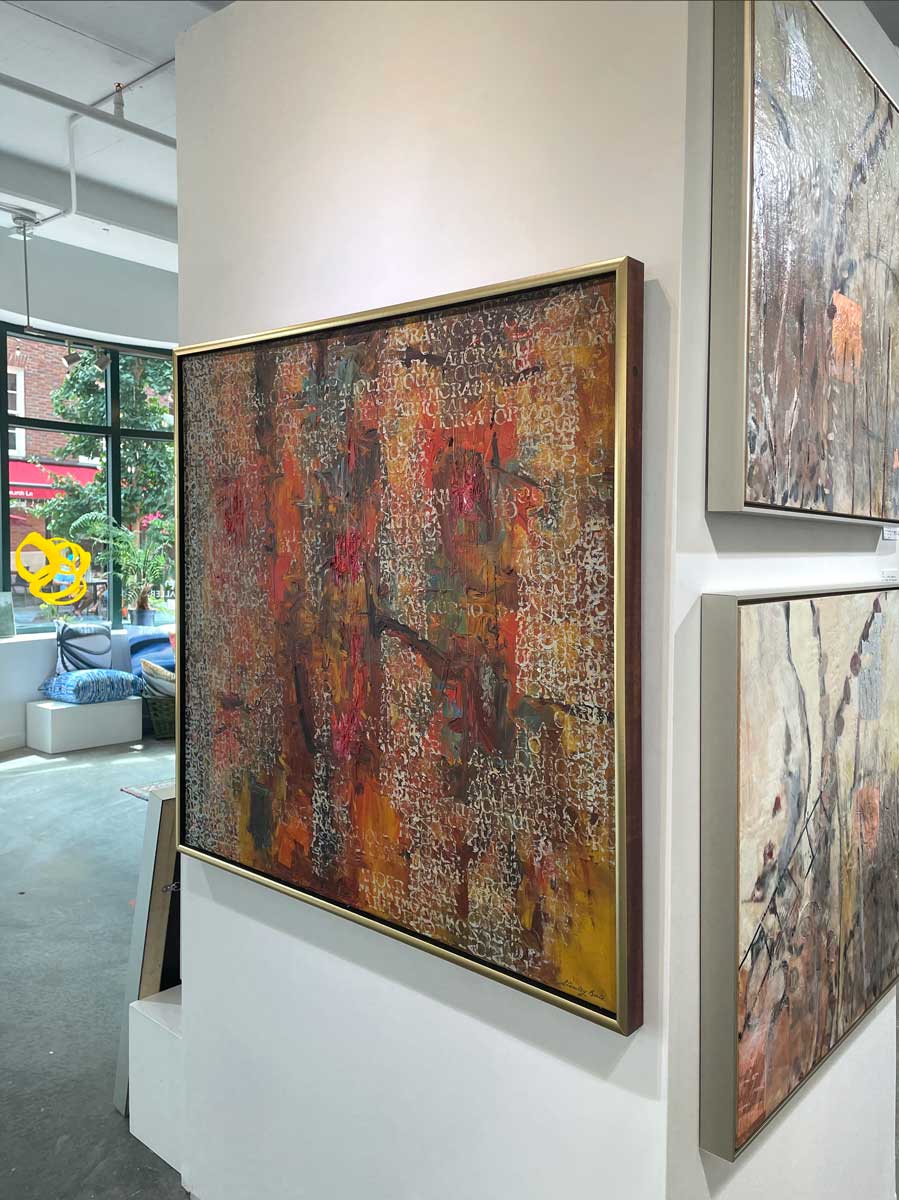 A right side-angle view of a multicolored abstract painting in a warm gold frame hangs on a white wall.