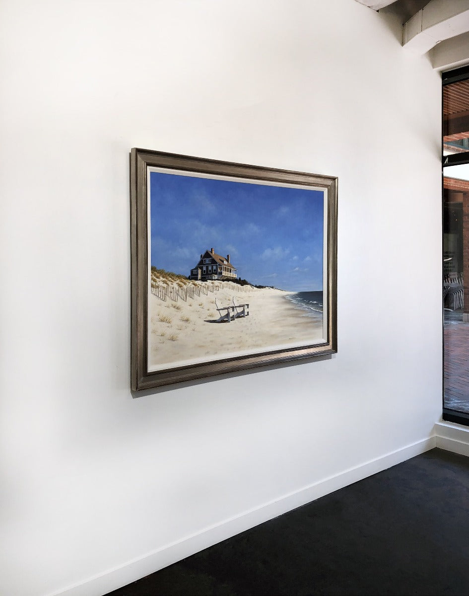 A left side-angle view of a painting of a realist coastal print framed on a white wall.