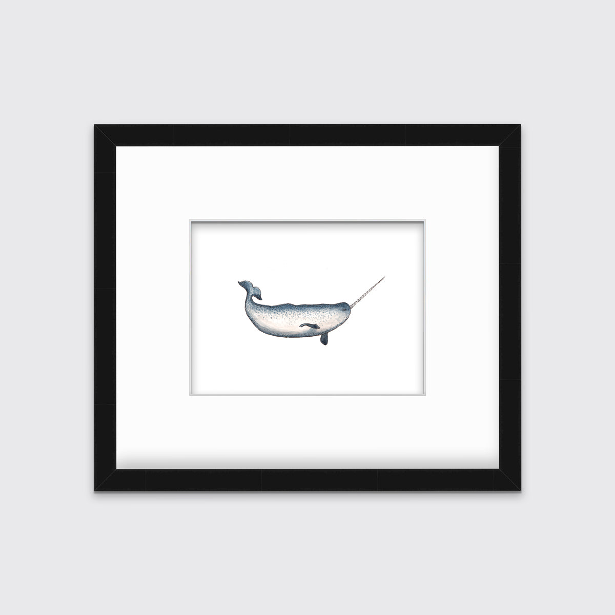 A blue and white narwhal print in a black frame with a mat hangs on a white wall.
