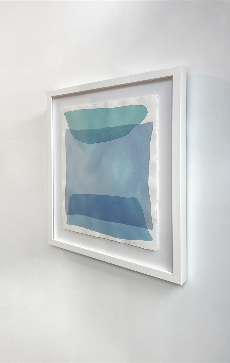 A right side-angle view of blue and green shapes overlap in this painting by Nealy Hauschildt in a white frame floating above a white matte hangs on a white wall.