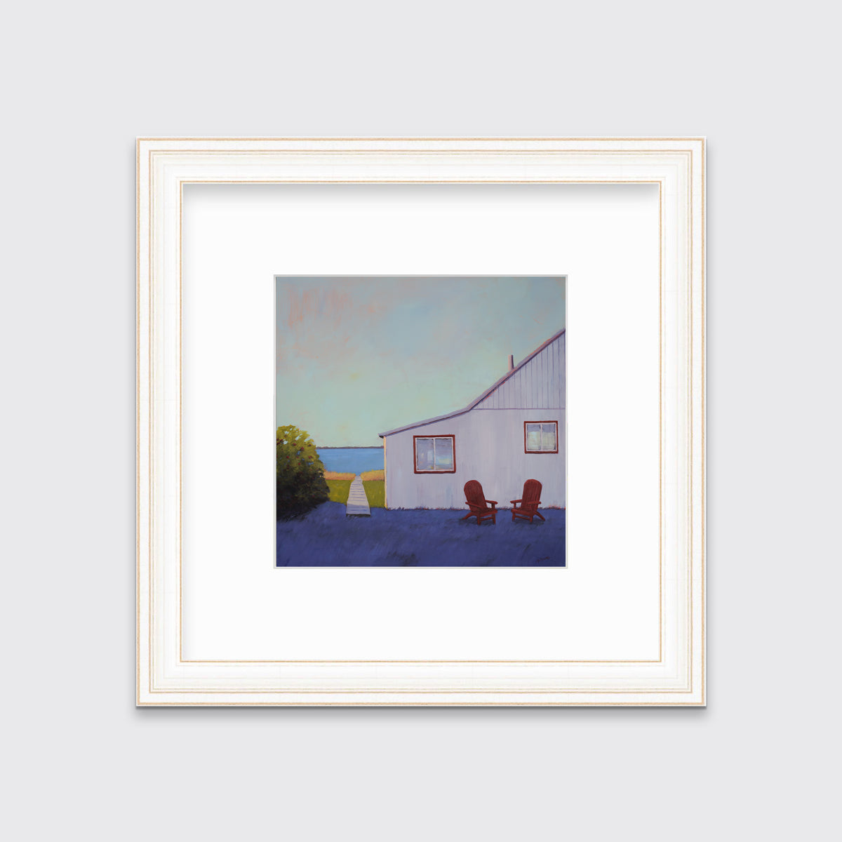 A blue, lavender and light purple contemporary seascape print with a beach house, two red adirondack chairs and a walkway leading to the water in a white and gold frame with a mat hangs on a white wall.