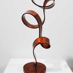 The back side of abstract, steel sculpture with orange dye, sitting on a pedestal in front of a white wall.