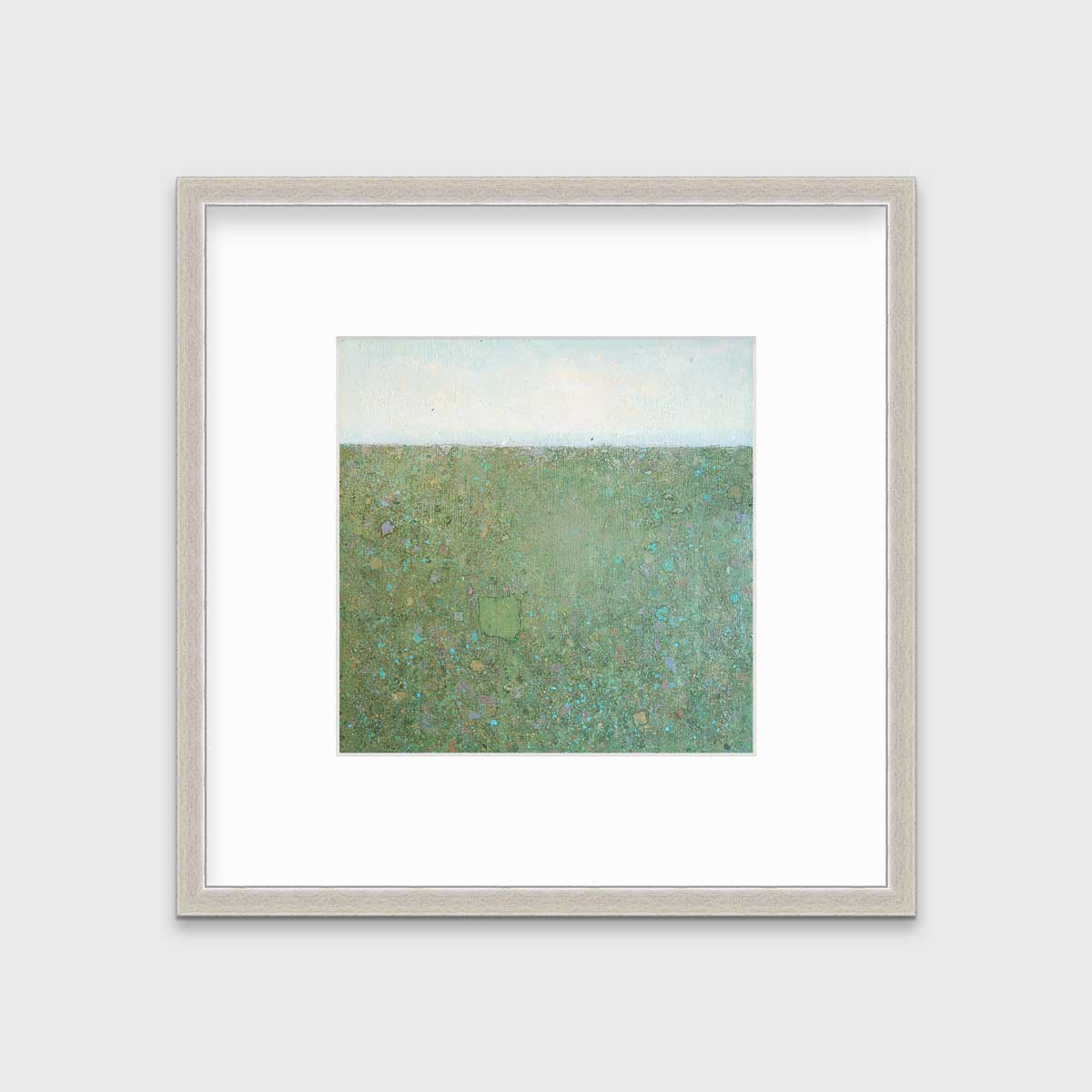 A green and blue abstract landscape print in a silver frame with a mat hangs on a white wall.
