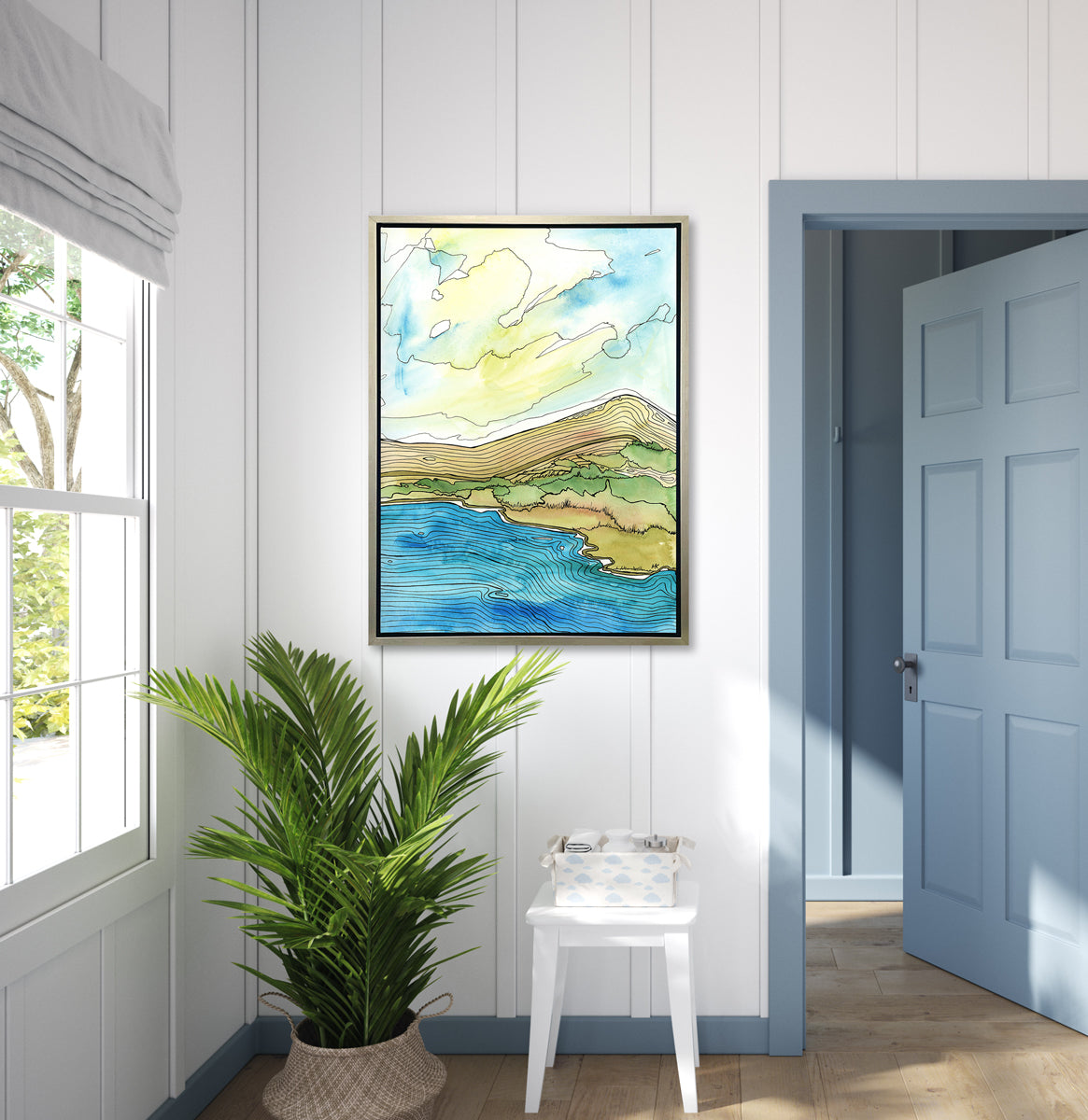 A blue, green, brown and light yellow abstract landscape with black outlines print in a silver floater frame hangs on a white wall above a potted floor plant, a white side table with baby accessories and next to a blue door.