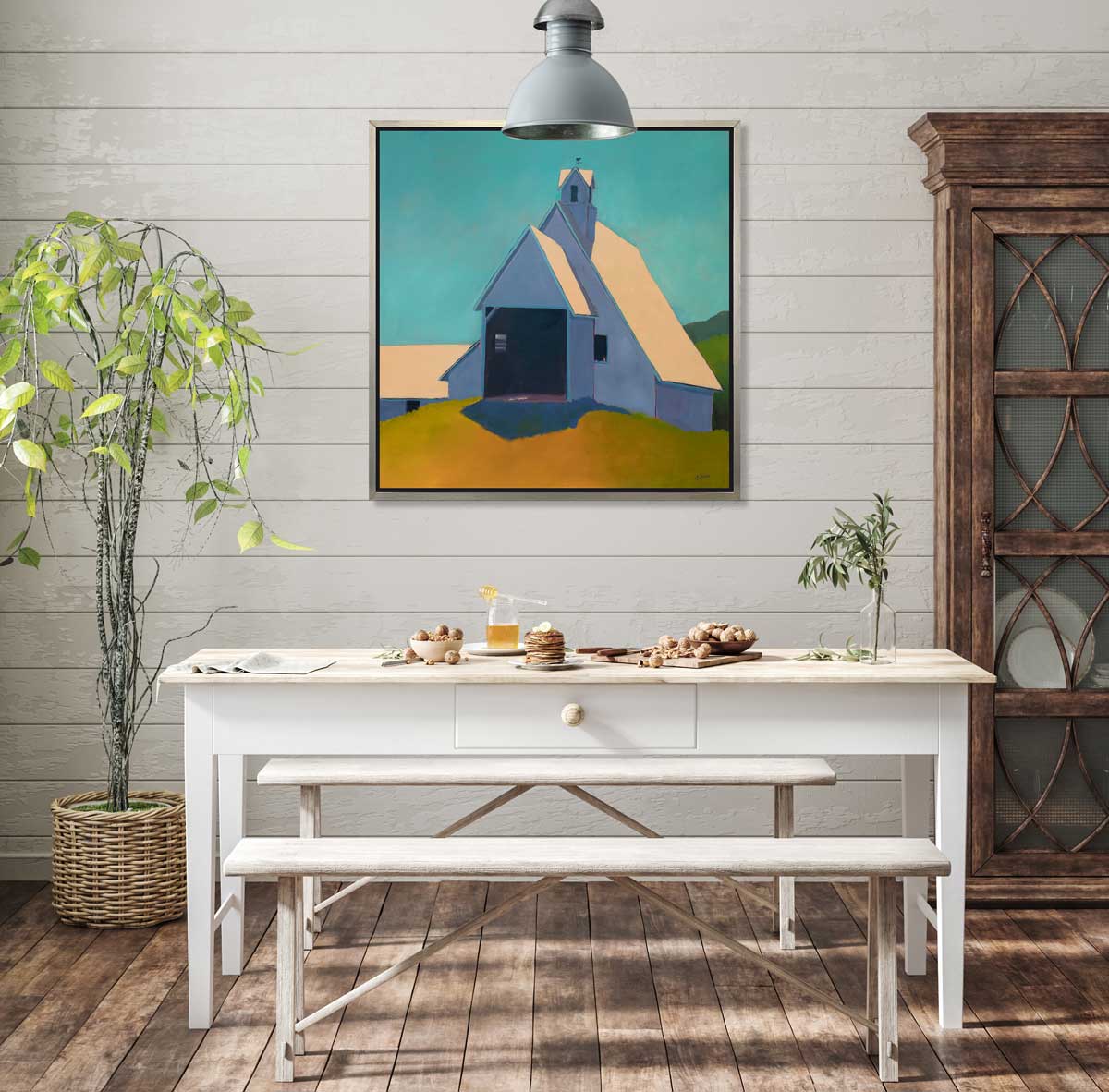 A teal, lavender, and peach contemporary barn print in a silver floater frame hangs on a shiplap white wall above a white table with a bowl of acorns, a plate of stacked small pancakes, and a cutting board with more acorns.