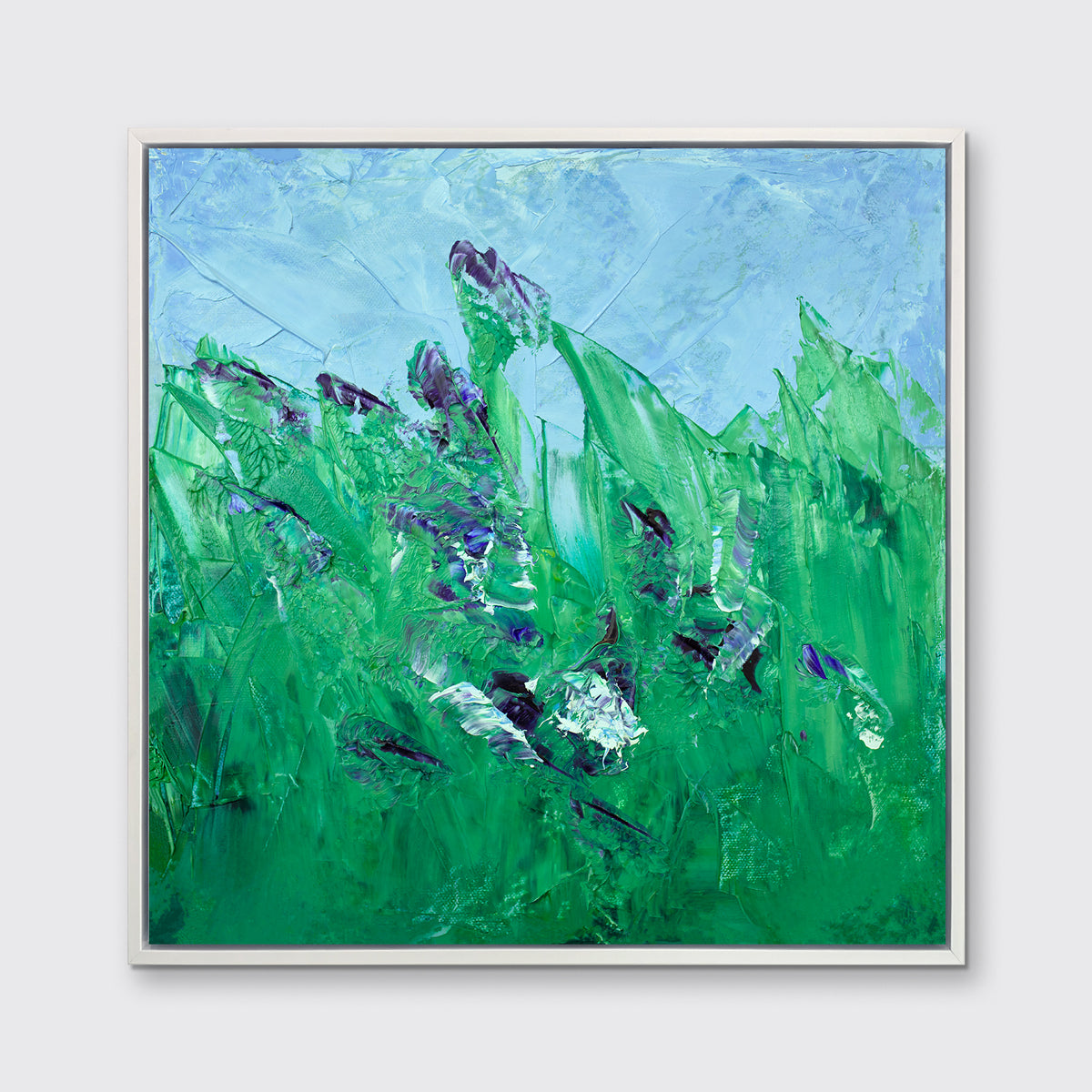 A blue and green abstract landscape print in a white floater frame hangs on a white wall.