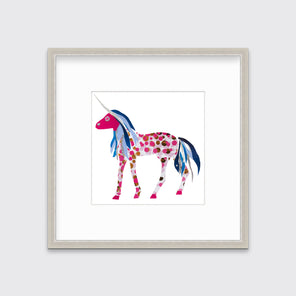 A white, pink, blue and silver collaged unicorn print in a silver frame with a mat hangs on a white wall.