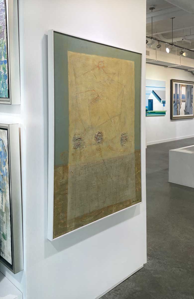 A left side-angle view of a teal, yellow and grey abstract painting in a white floater frame hangs on a white wall.