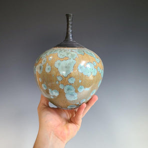 A beige and teal porcelain vessel with a narrow matte black neck.