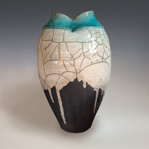 A textured white and grey glazed vessel with a teal large opening sits on a white surface.