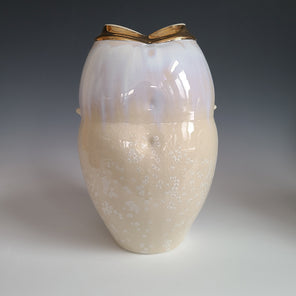 A white and cream crystalized glazed vase with two faux handles and a wide gold opening sits on a white surface.