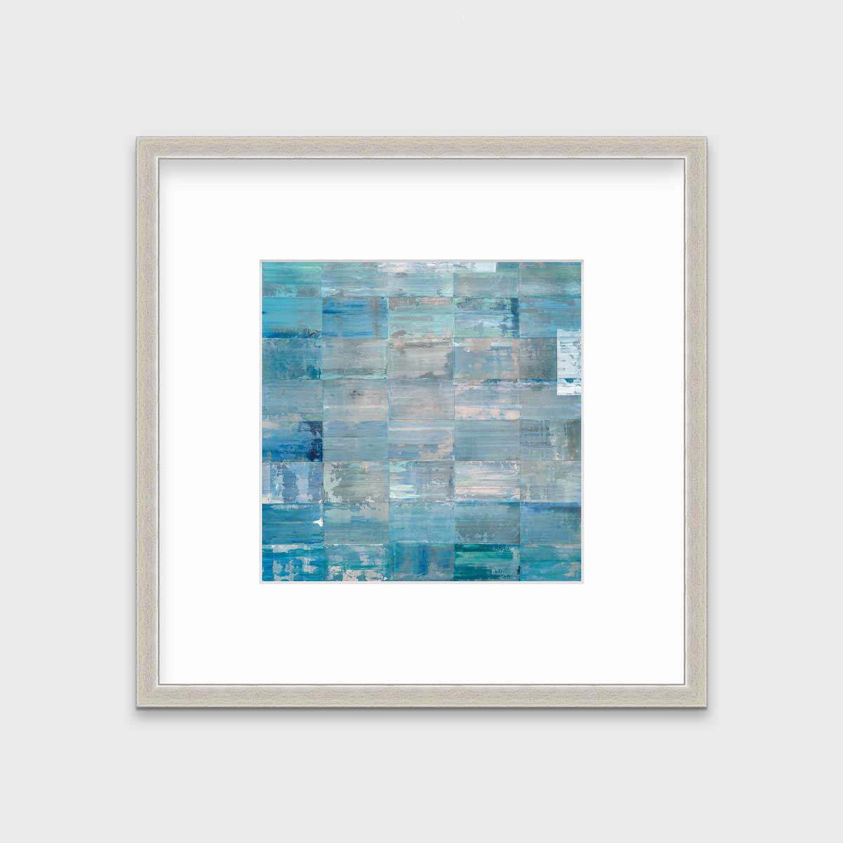 A blue and teal geometric print by Ned Martin in a silver frame with a mat hangs on a white wall.