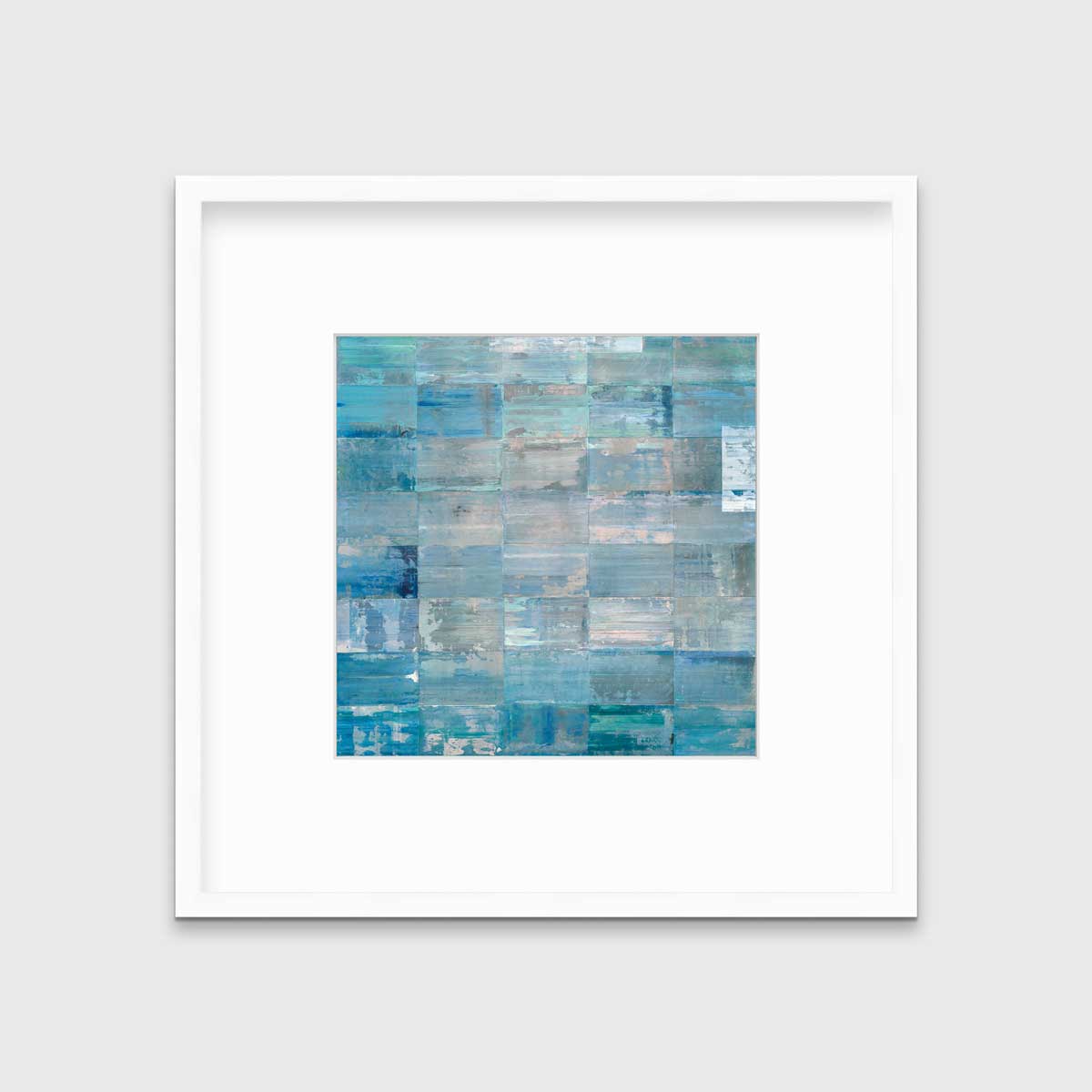 A blue and teal geometric print in a white frame with a mat hangs on a white wall.