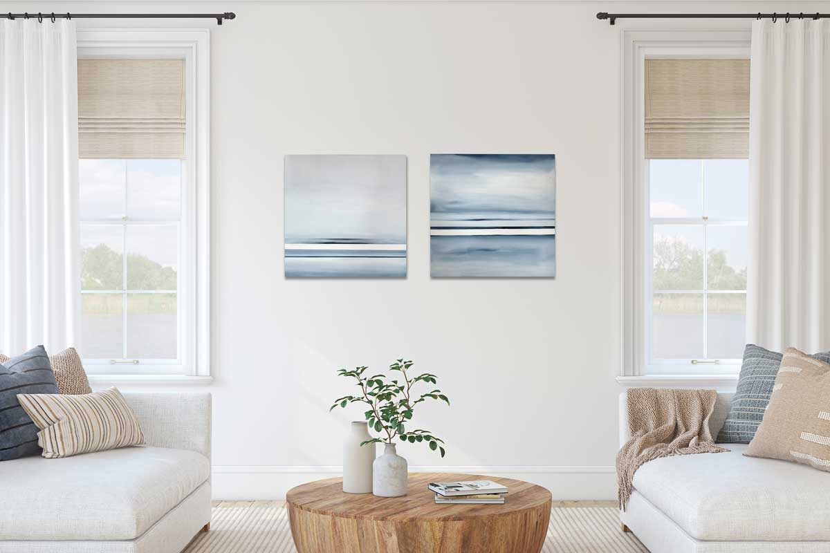 Two abstract paintings hang side by side, each of different blue, grey and white horizontal line placement. They hang on a white wall in between two windows and two sofas.