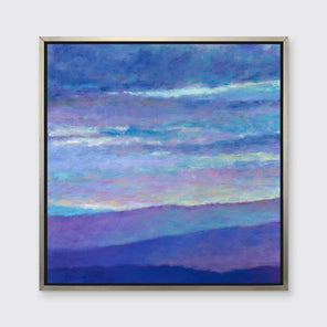 A blue, purple and light yellow abstract landscape print in a silver floater frame hangs on a white wall.