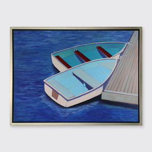 A blue, light blue and beige contemporary nautical print of two docked rowboats in a silver floater frame hangs on a white wall.