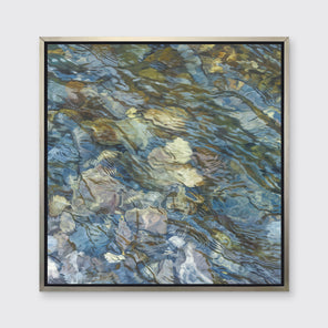 An abstract river bed print in a silver floater frame hangs on a white wall.
